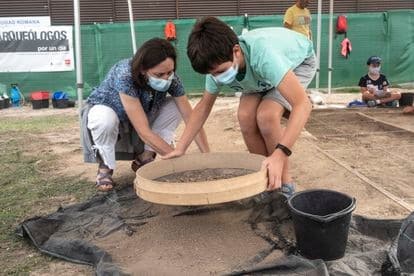Una madre, María García, arqueóloga que participó en las primeras excavaciones, ayuda a su hijo Aarón a cribar la tierra por si quedaran restos que han pasado inadvertidos.